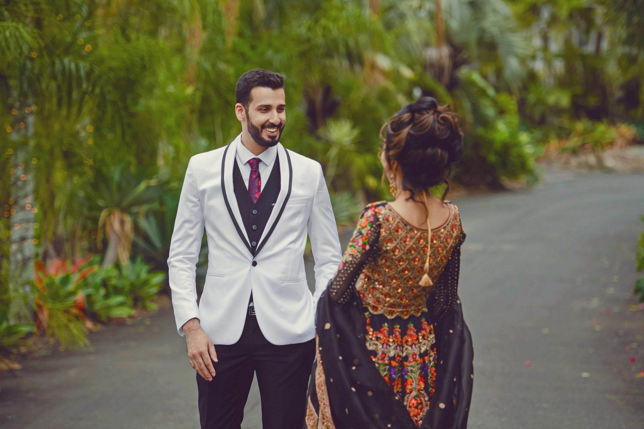 A groom is smiling to his bride with his white wedding suit