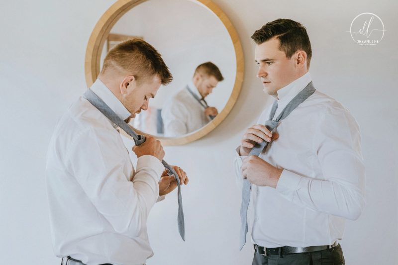 groom and his groomsmen fixing their necktie in front of a mirror