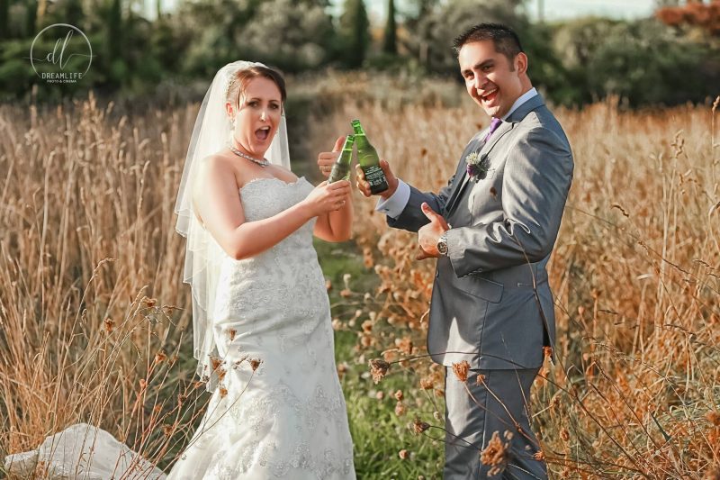 groom and bride holding a bottle of beer in an open grassland