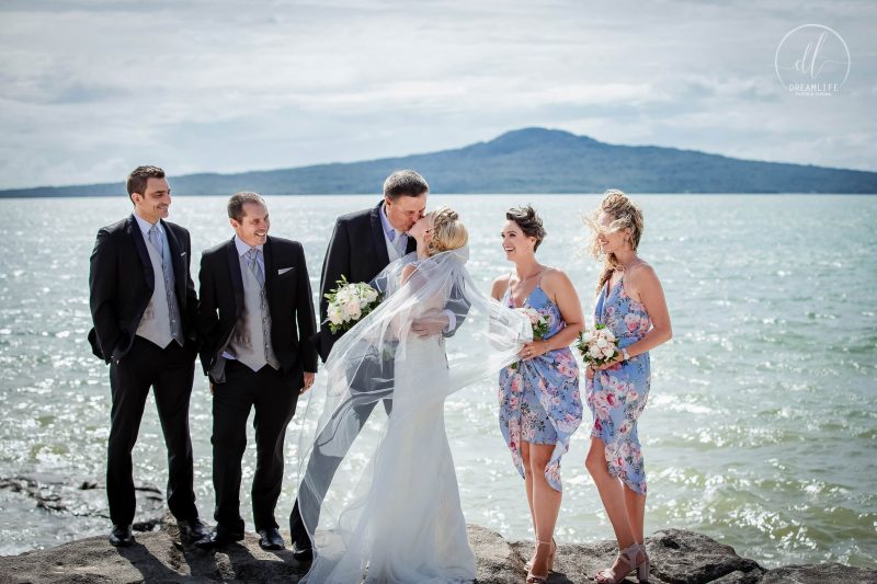 groom and bride with their brides maid and groomsmen in an open sea and mountain backdrop