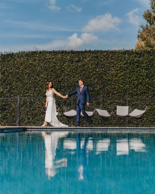 bride holding her groom hands in a plant wall backdrop in pool