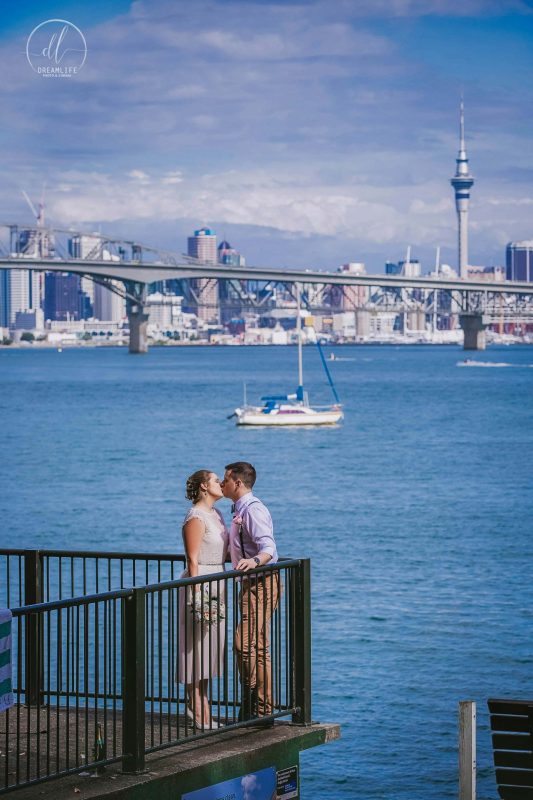bride and groom kissing in a seaside with auckland city backdrop