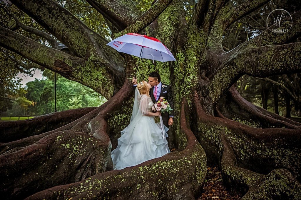 groom and bride holding an umbrella in a rainforest backdrop
