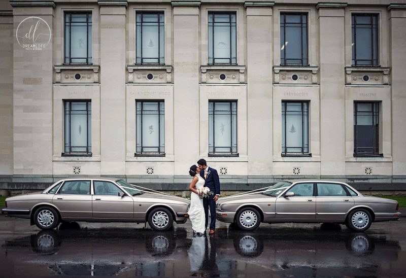 bride and groom with car and a building backdrop