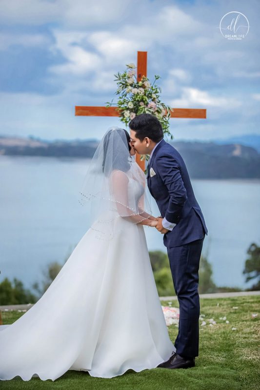 bride and groom in a wedding ceremony venue with a wooder cross and open sea backdrop