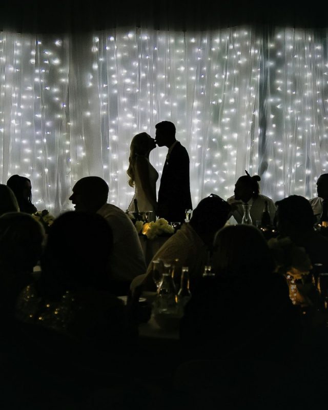 silhouette of bride and groom kissing in a wedding venue in front for their wedding guests