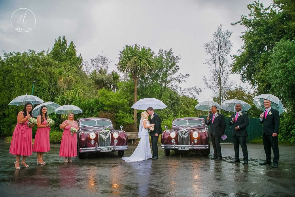 bride and groom in a rainy day wedding with their entourage