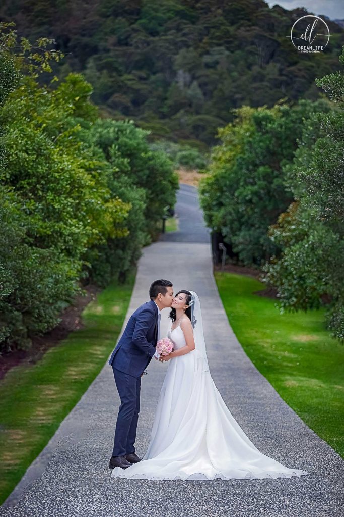 groom and bride kissing in the middle of the road with trees backdrop